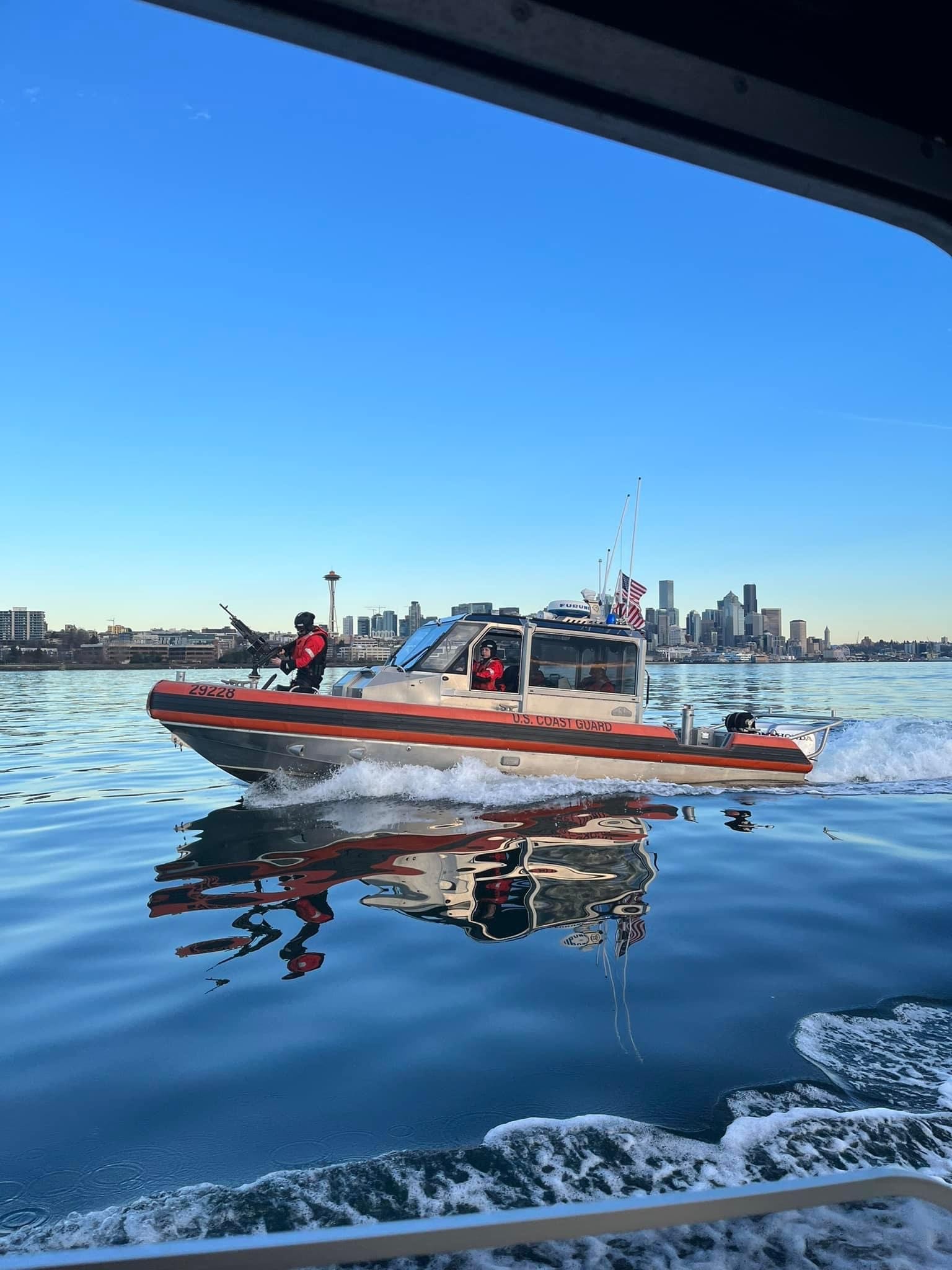 A U.S. Coast Guard response boat underway on the water with the Seattle skyline and an American flag behind it